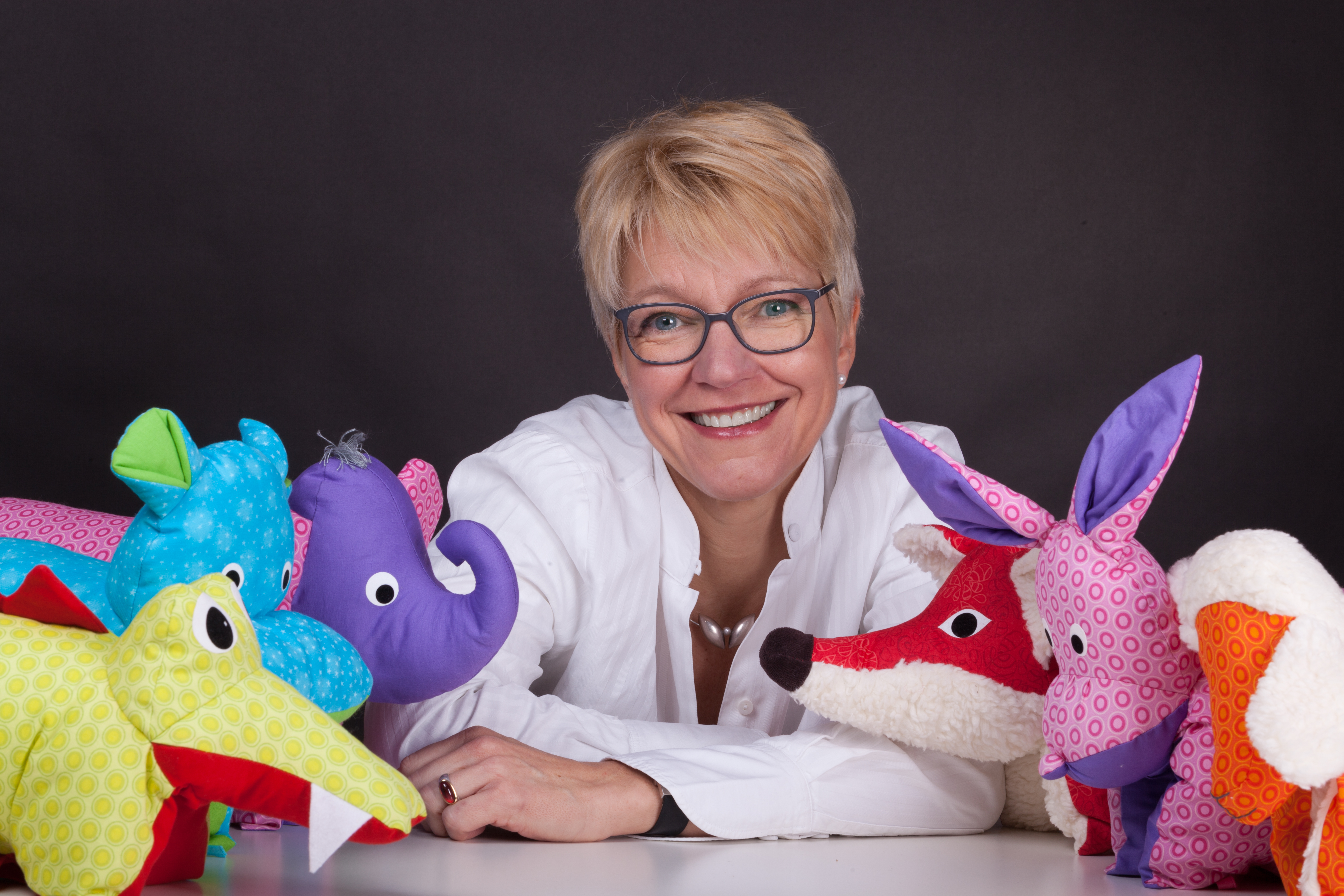Flosinn Inhaberin Nicole Kettler umgeben von farbenfrohen Tierkissen Fuchs, Nilpferd, Elefant, Krokodil, Hase, Lamm
